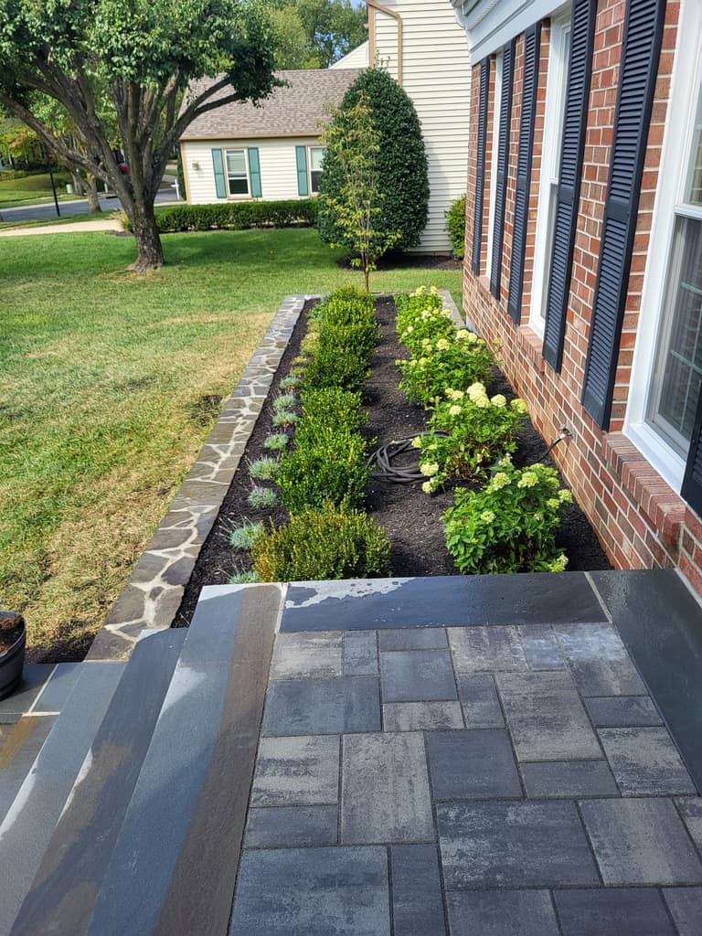 Hydrangeas and boxwood filling the raised bed above the stacked-stone wall, beside the new landing