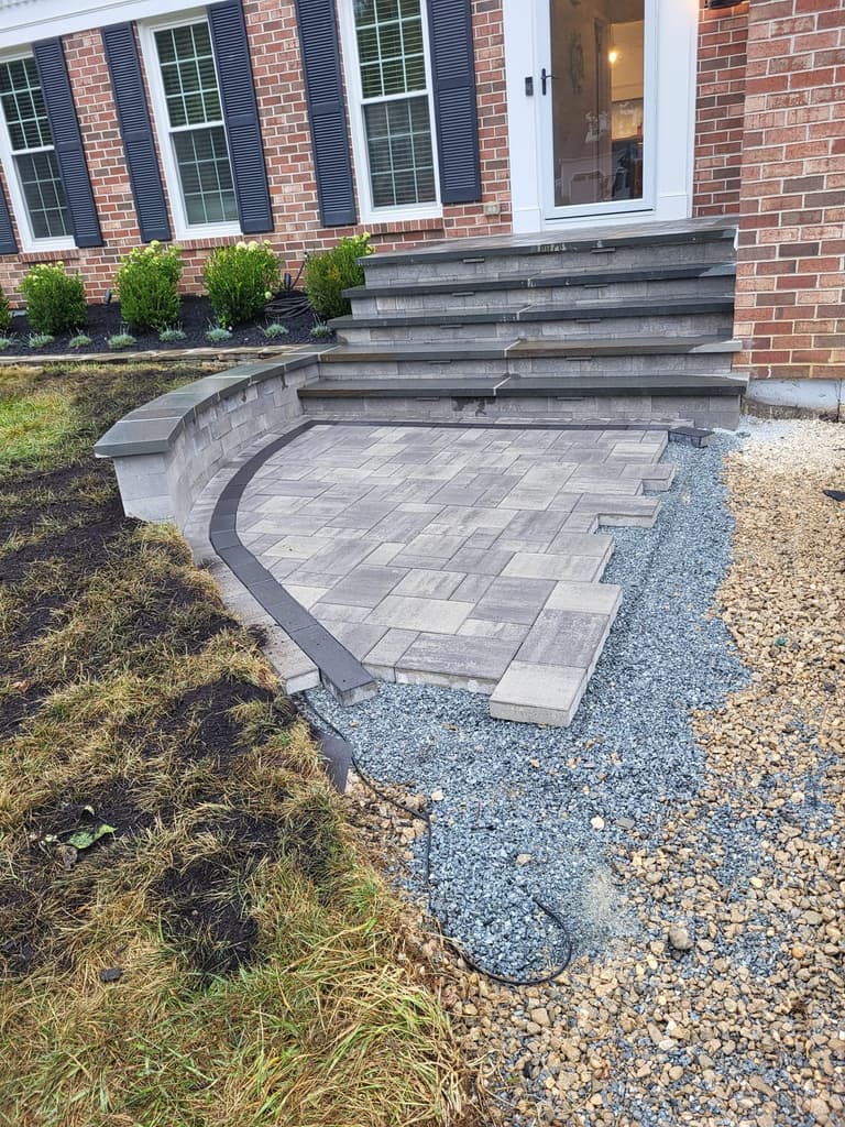 During — the large-format paver landing laid out with its soldier-course border, gravel still open around the edge