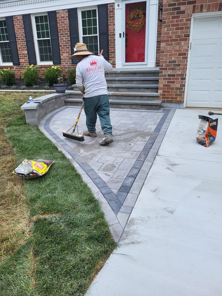 During — a King Cuts crew member sweeping polymeric sand into the joints of the finished paver landing