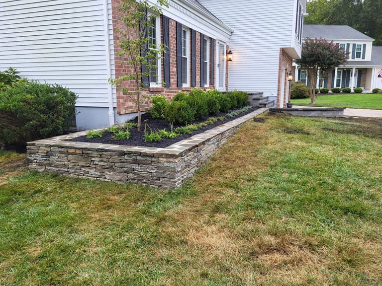 During — the stacked-stone planter wall filled and planted along the front of the house