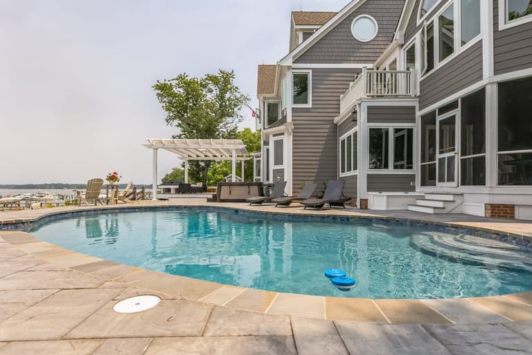 The white pergola and its seating area at the far end of the pool deck