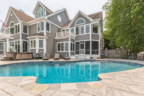 The rear of the house across the pool, with the spa and loungers on the paver deck