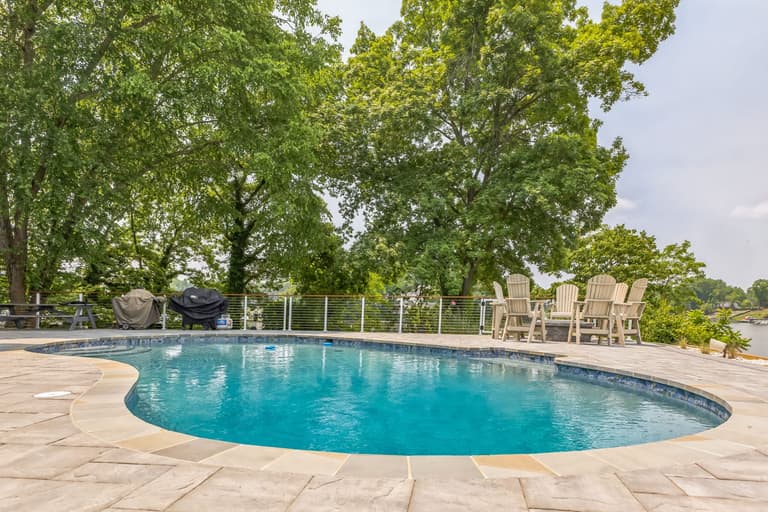 Mature trees shading the far side of the pool deck above the shoreline
