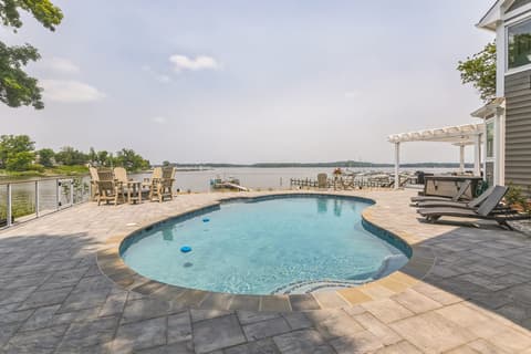 The freeform pool and paver deck looking out over the water, with the pergola beyond