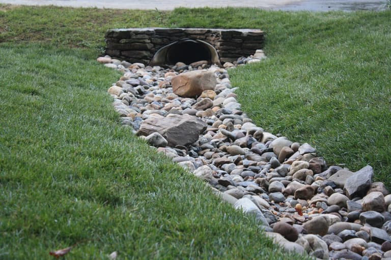 River-rock dry creek bed with boulders carrying drainage across a lawn