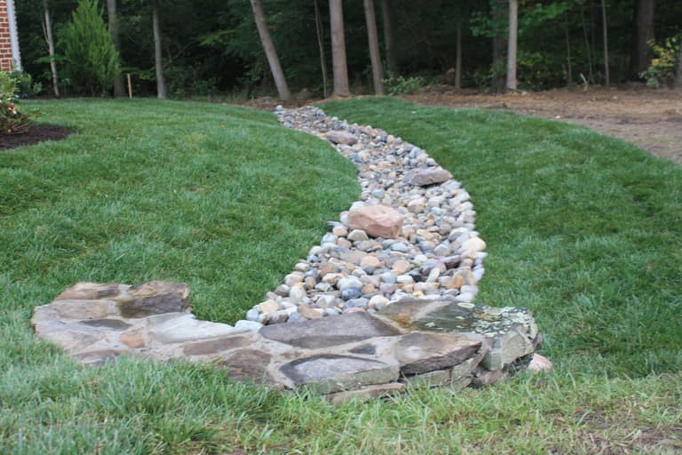River-rock dry creek bed carrying drainage across a lawn