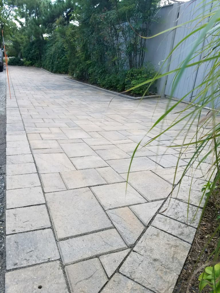 Large-format paver driveway running alongside a fence line in Riva