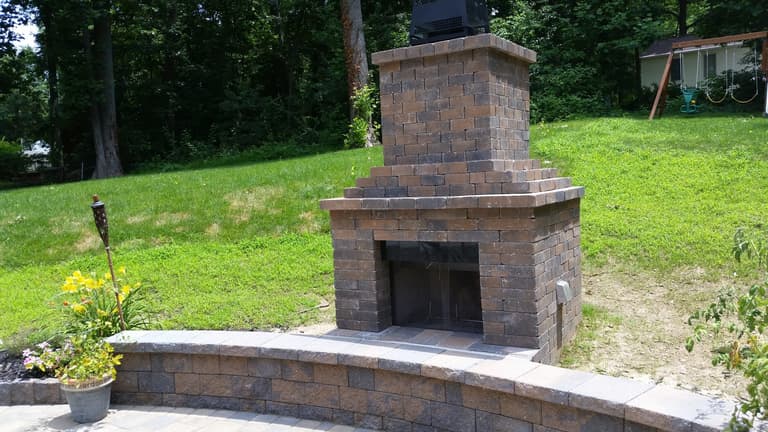 Tall paver outdoor fireplace with a hearth and seat wall