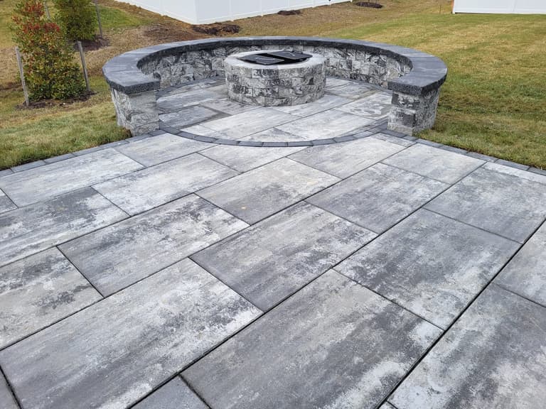 Round paver fire pit ringed by a curved seat wall on a grey large-format paver patio