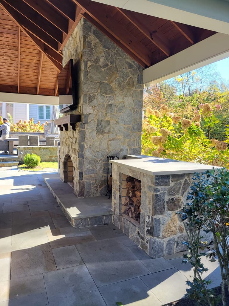 Stone outdoor fireplace and built-in wood box on a bluestone patio