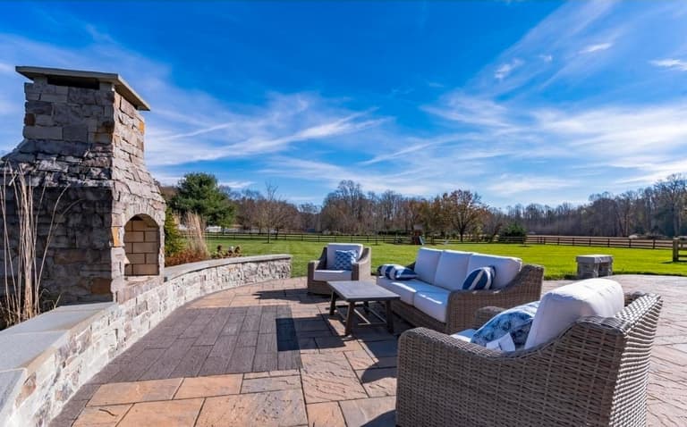 Stacked-stone outdoor fireplace and curved seat wall beside wicker lounge seating on a paver patio