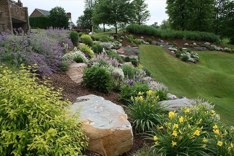 Terraced hillside garden with boulders, ornamental grasses, and mixed perennial beds