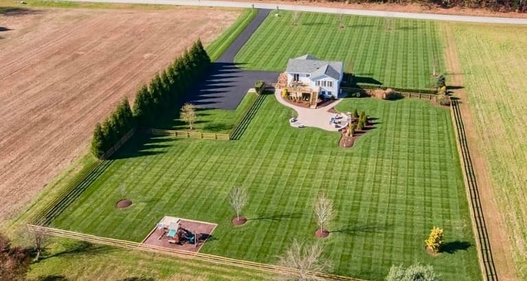 Aerial of a whole fenced property with striped lawns, young trees and planting beds