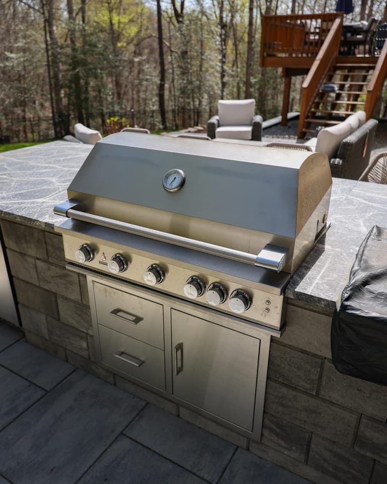 Built-in stainless grill set into a stone island with a stone countertop on a paver patio