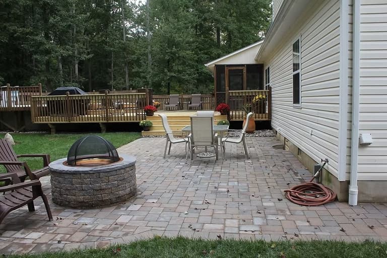 Paver patio with a round stone fire pit and dining set beside a raised deck