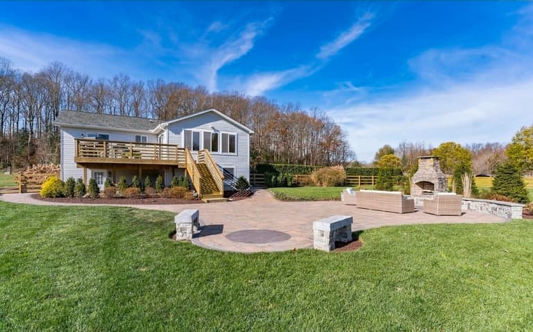 Paver patio with stone benches, a fire-pit inlay and an outdoor fireplace, seen across the lawn