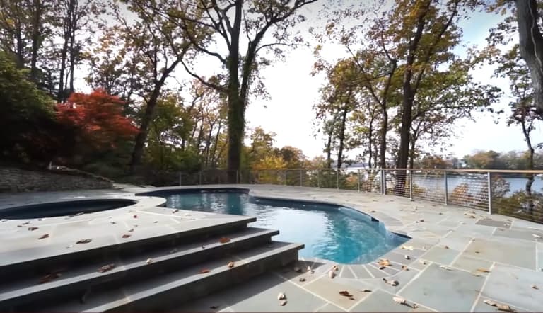 Freeform pool with a bluestone deck and glass railing in autumn