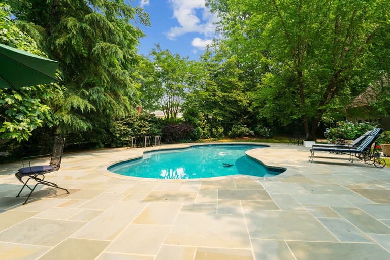 Freeform pool with a flagstone deck in a wooded backyard