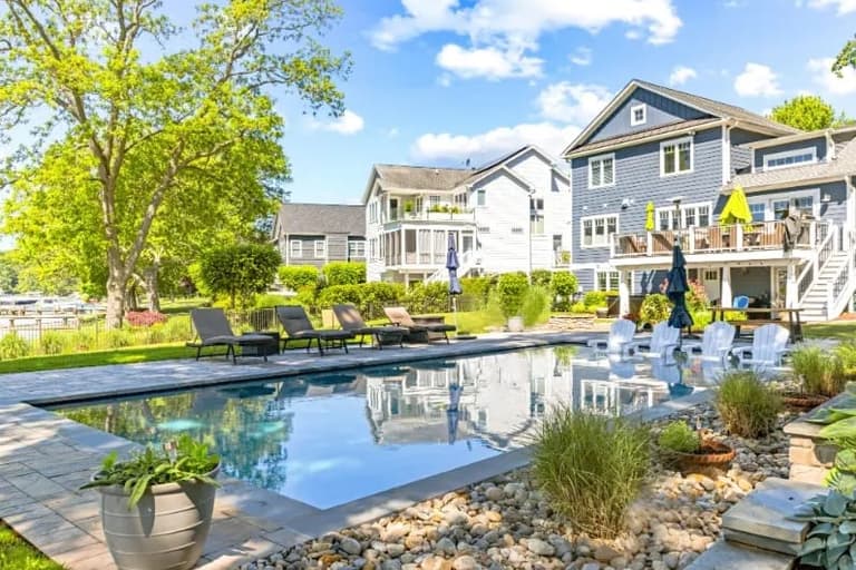 Rectangular pool reflecting the sky beside a paver deck and plantings