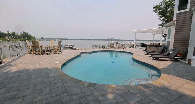 Freeform waterfront pool with a paver deck, pergola, and water view