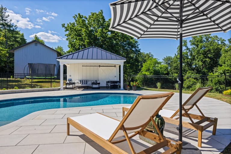 Poolside lounge chairs and a striped umbrella on the paver deck