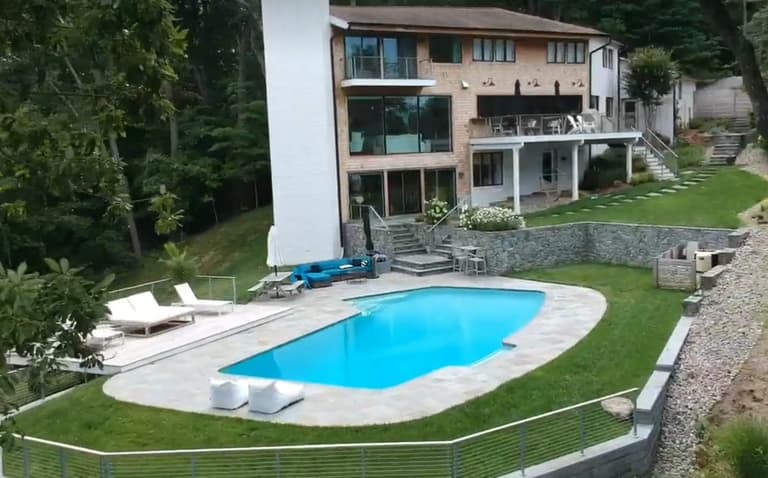 Stone pool deck with an integrated retaining wall and glass railing