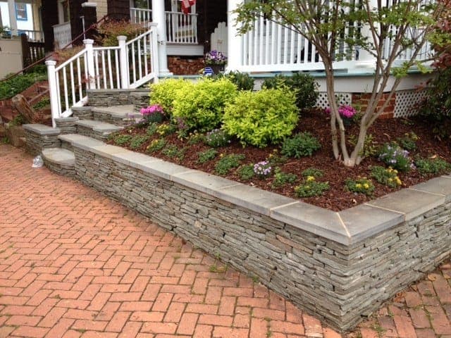 Low stacked-stone seat wall with a bluestone cap holding a front planting bed above a brick walkway