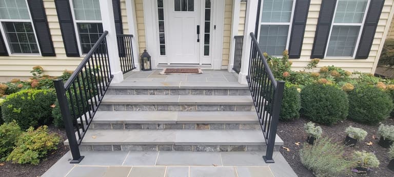 Bluestone front steps with stone-veneer risers and black metal railings up to a front porch