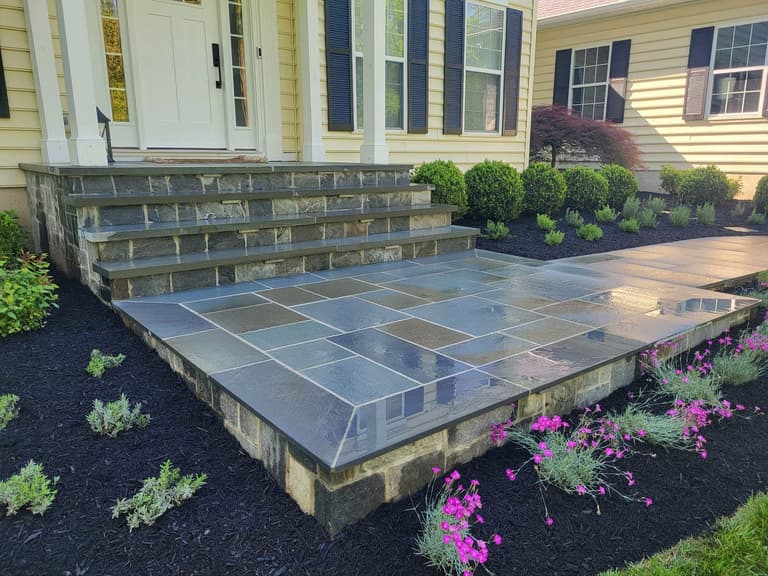 Raised bluestone entry landing and steps with stone-veneer risers, edged with new plantings