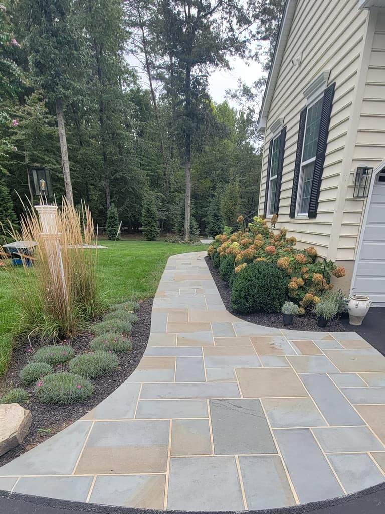 Bluestone walkway meeting the driveway beside the garage, bordered by hydrangeas and ornamental grasses