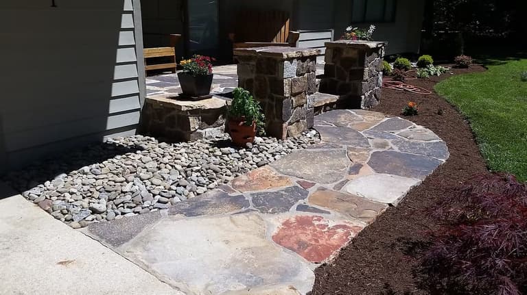 Flagstone walkway and stone steps up to a front porch, edged with a river-rock bed